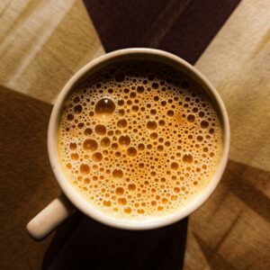 Close-up of frothy milk tea in a cup on a geometric patterned tablecloth.